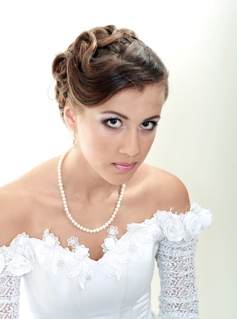Beautiful young woman in white dress and pearl necklace beige backgroundの写真素材