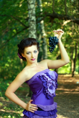beautiful young woman in violet fashion dress holding dark blue grapesの写真素材