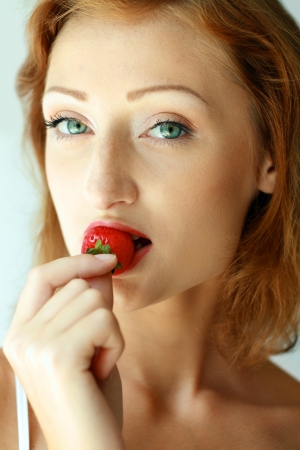 beautiful young woman face enjoying strawberries in morning lightの写真素材