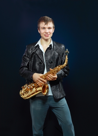 Studio portrait of happy young man with saxophone on dark background.の写真素材