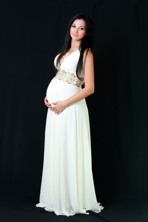 beautiful pregnant woman in long white dress over dark backgroundの写真素材