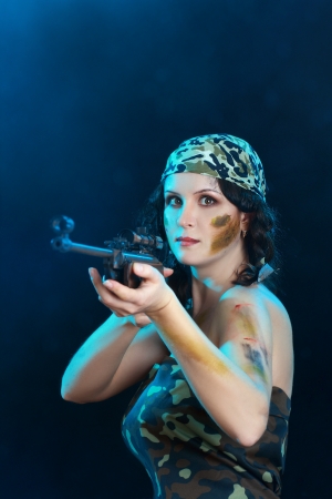 Beautiful woman holding weapon weared camo over dark backgroundの写真素材