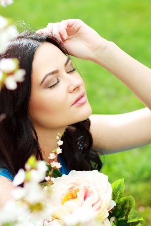 beautiful happy brunette woman in the park on a warm spring day with blossom flowers around herの写真素材