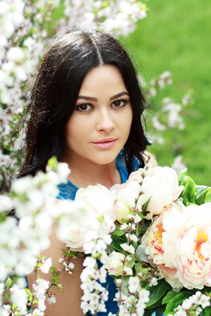 beautiful happy brunette woman in the park on a warm spring day with blossom flowers around herの写真素材