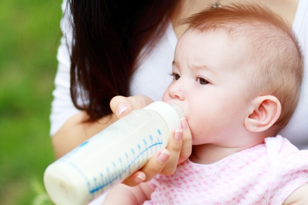 Beautiful young mother is feeding her baby from a bottle outdoorの写真素材