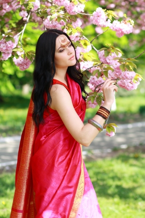 beautiful asian indian woman in the park on a warm spring day with blossom flowers around herの写真素材
