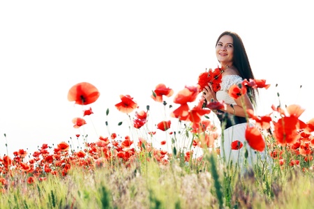 beauty woman in poppy field in white dress in a sunny summer dayの写真素材