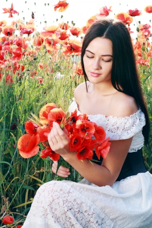 beauty woman in poppy field in white dress in a sunny summer dayの写真素材