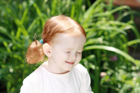 Cute little girl on the meadow in summer day closed eyes because bright lightの写真素材