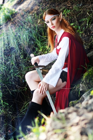 Elf girl on the rock in red cloak posing outdoorの写真素材