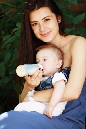 Beautiful young mother is feeding her baby from a bottle outdoorの写真素材