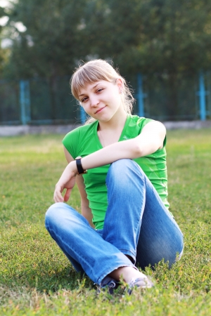 young blond woman sitting on grass at summer green park.の写真素材