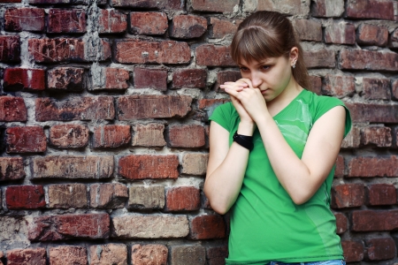 Sad young woman near stone wall. Dark depressive colors. Teenage problemsの写真素材