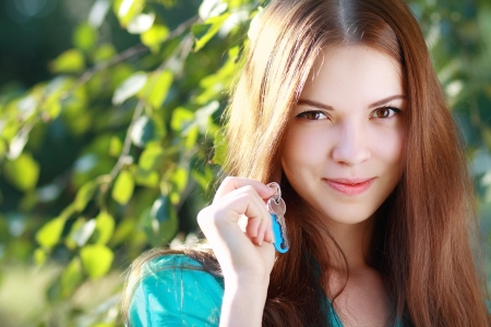 beautiful smiling young woman holding up a set of keys belonging to her house in her hand outdoor in green park の写真素材