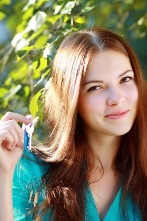 beautiful smiling young woman holding up a set of keys belonging to her new house in her hand outdoor in green parkの写真素材