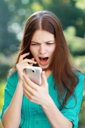 anxcios young girl looking at phone seeing bad news or photos there with disgusting emotion on her faceの写真素材