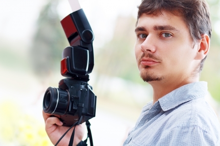 young man photographer with black professional camera and mobile flashの写真素材