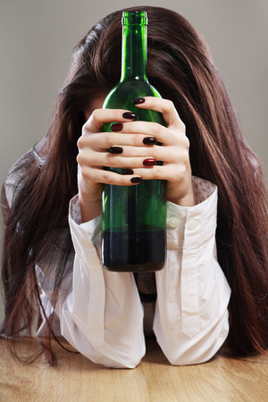 Young beautiful woman in depression, drinking alcohol hold bottle in her hands and hiding her faceの写真素材