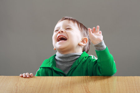 Portrait of happy laughing little boy sitting on the desk overjoyの写真素材