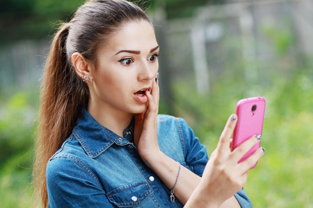 anxcios young girl looking at phone seeing bad news or photos there with disgusting emotion on her faceの写真素材