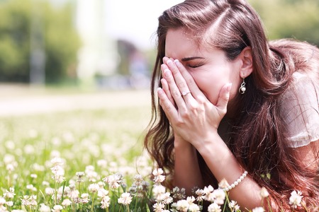 Pollen allergy, girl sneezing in a field of flowersの写真素材