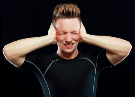 stressed young man close his ears and eyes on dark background
