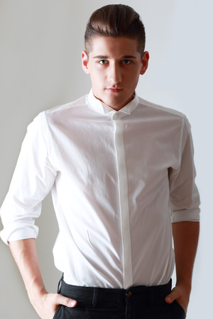 Fashion portrait of young man in white shirt poses over wall with contrast shadowsの写真素材