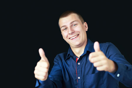 Portrait of smart man smiling and show giving you two thumbs up on dark studio backgroundの写真素材