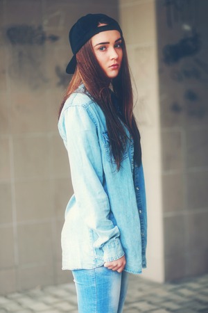 Lonely teenage girl standing alone near concrete wall in urban environment.の写真素材
