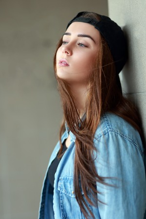 Lonely teenage girl leaning against concrete wall in urban environment.の写真素材