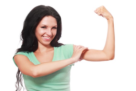 A happy beautiful girl is holding up her strong muscles on an isolated background to show confidence and strength.の写真素材