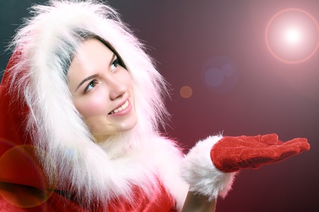close up portrait of a smiling beautiful happy girl in christmas santa hat. beauty woman. show palm under light beakon happy new year 2016.の写真素材
