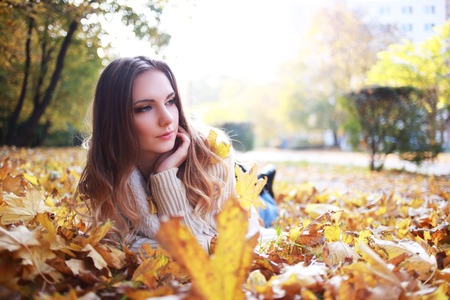 Image of cheerful young woman laying down on the ground covered dry autumnal foliage in beautiful parkの写真素材