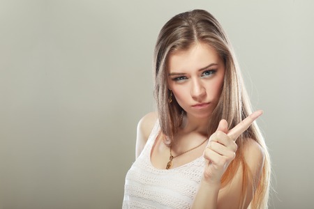threatening 20s blonde girl showing her index finger for signal of stopping, forbidding or behaving with unhappinessの写真素材