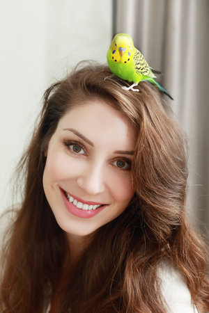 beautifl smiling woman with green parrot on her head beloved pet