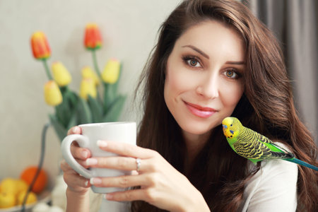 beautiful smiling woman with green parrot on her head beloved pet