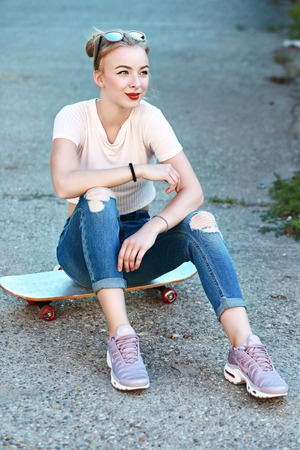 full length portrait of young girl relaxing sitting on her board on the streetの写真素材