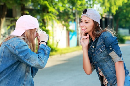 A woman takes pictures of another young woman on the camera, outdoors, recreation, entertainmentの写真素材