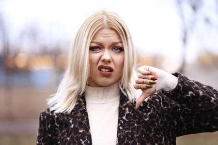 portrait of young blond woman showing thumbs down walking on the street in sunsetの写真素材