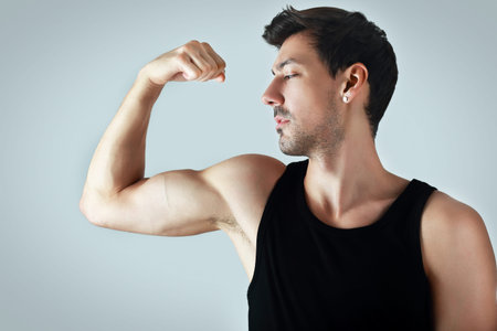 handsome athletic young man showing his biceps posing next to color background in photostudio