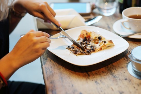 Woman eating vegetarian pizza in a pizzeria restraurant (Selective Focus, Focus on the pizza slice)の写真素材