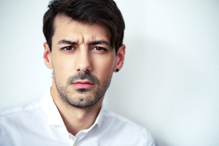 close up portrait of young serious handsome man wearing white shirt looking with suspicion at camera...