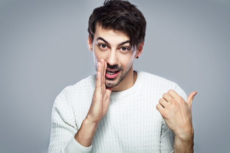 young handsome man dissolves gossip standing next to color background in photostudio