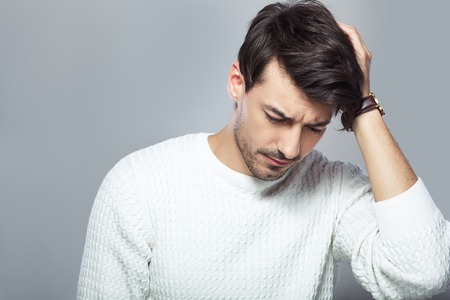 portrait with young stressed man lowered his head keeping hand near head standing next to the color backgroundの写真素材