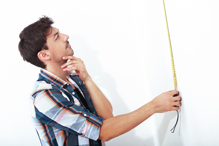 half length portrait of young man with tape measure doing repairs standing next to white backgroundの写真素材