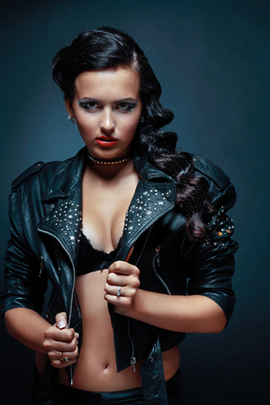 portrait of young passionate brunette in leather jacket standing next to color backgroundの写真素材