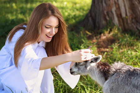 young woman walking in nature  in white dress feeling happy holding goat by the horns