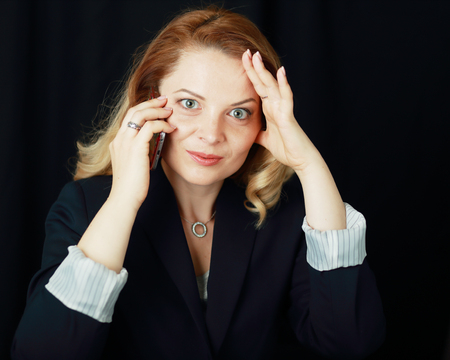 amazed business woman calling on cell phone and looking shocked over dark backgroundの写真素材