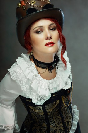 portrait of beautiful steampunk woman wearing vintage hat and corset posing next to color backgroundの写真素材
