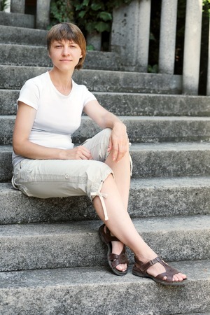 normal woman sitting on stone stairs in sunny dayの写真素材